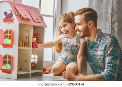 Happy father and daughter girl play with doll house at home. Funny lovely family is having fun in kids room.