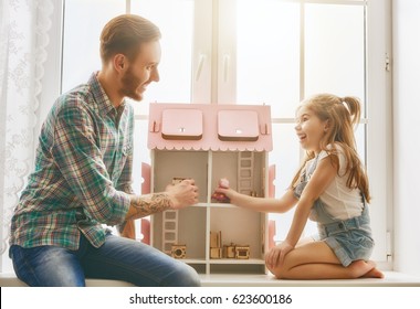 Happy Father And Daughter Girl Play With Doll House At Home. Funny Lovely Family Is Having Fun In Kids Room.