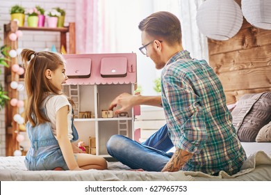 Happy Father And Daughter Girl Play With Doll House At Home. Funny Lovely Family Is Having Fun In Kids Room.