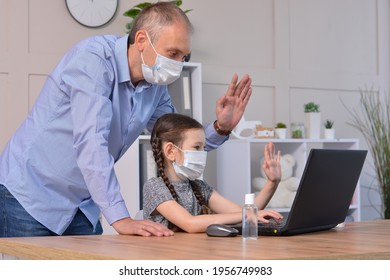 Happy Father And Daughter In Medical Masks Greet With Friends Or Teacher Via Laptop During Coronavirus Pandemic. Online Communication, Training, Social Distance, Stay At Home, Homeschooling Concept