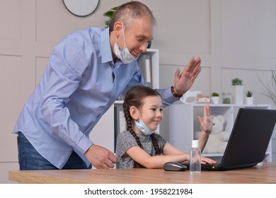 Happy Father And Daughter In Medical Masks Greet With Friends Or Teacher Via Laptop During Coronavirus Pandemic. Online Communication, Training, Social Distance, Stay At Home, Homeschooling Concept