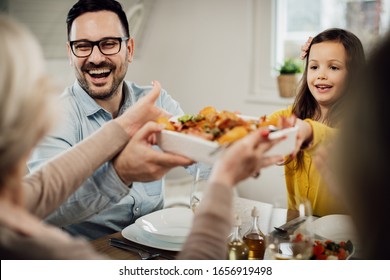 Happy Father And Daughter Serving Food While Having Family Lunch At Dining Table At Home. 