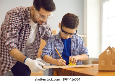 Happy Father Day And Childhood Concept. Father Handyman And Boy Son Child Work With Hand Tools Using Ruler And Pencil Making Plank Roof For Birdhouse At Family Carpentry Home Workshop