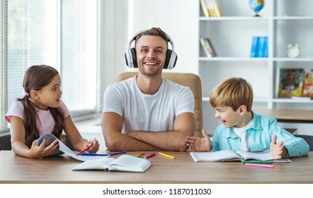 The happy father in headphones sitting with kids at the desk - Shutterstock ID 1187011030