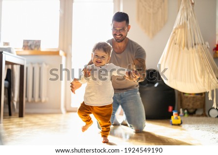 Happy father helping little son walking in living room
