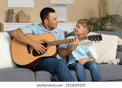 Happy father with his little son playing guitar on sofa at home - Powered by Shutterstock