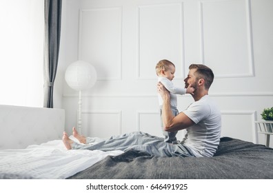 Happy Father With His One Year Old Son Playing At Home On The Bed