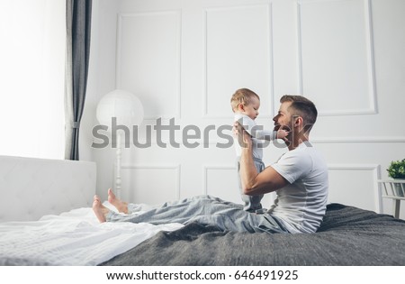 Happy father with his one year old son playing at home on the bed