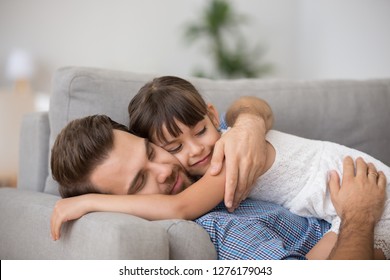 Happy father hugging cute little girl lying together resting on comfortable sofa, smiling dad embracing kid daughter cuddling enjoying healthy daytime nap at home, daddy and child relaxing on couch - Powered by Shutterstock