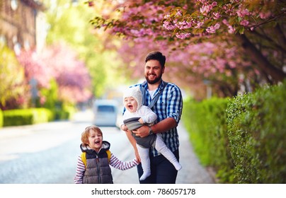 happy father with kids on the walk in spring city, baby carrier, paternal leave