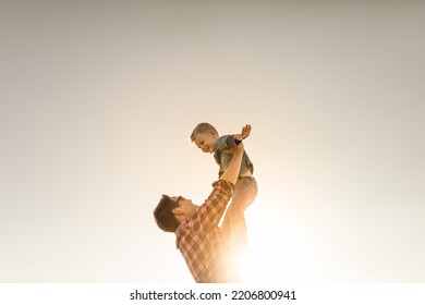 Happy Father Lifting His Son Child Up To The Sky. Fatherhood Concept. 