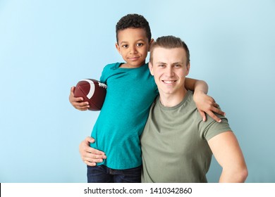 Happy father and little adopted boy with rugby ball on color background - Powered by Shutterstock