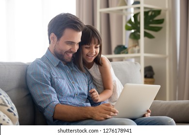 Happy Father And Little Daughter Laughing Watching Funny Video Using Laptop, Cheerful Dad And Child Girl Having Fun Playing Online Game On Sofa Together, Daddy With Kid Relaxing At Home With Computer