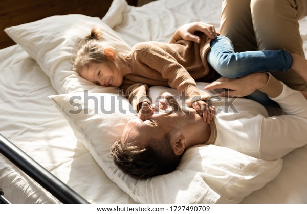 Happy father and little daughter relaxing in cozy\
bed together, smiling dad having fun with cute preschool girl,\
resting, taking nap in bedroom, family spending weekend together,\
enjoying free time