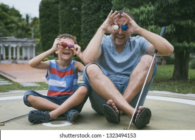 Happy Father And  Little Son Playing Mini Golf  In A Park At The Day Time. People Having Fun Otdoors. Concept Of Good Leisure.