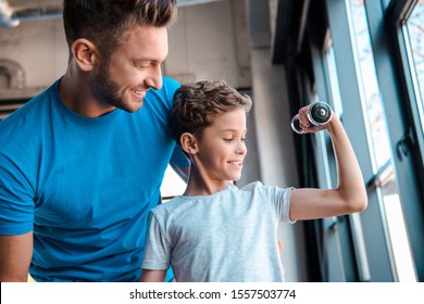 happy father looking at cheerful son exercising with dumbbell