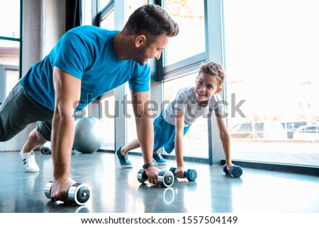 happy father looking at cheerful son and exercising with dumbbells