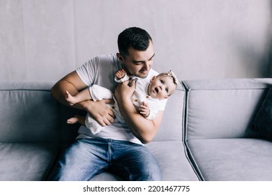 Happy Father Lying On Sofa Holding Baby Girl, Playing, Smiling. Side View.