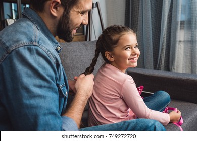 happy father making hair braid for daughter while sitting on couch at home - Powered by Shutterstock