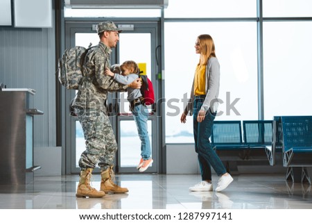 happy father in military uniform holding in arms daughter near wife in airport 
