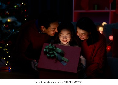 Happy father, mother and daughter opening and holding Christmas gift box while sitting on sofa at home. Happy Asian family on Christmas day. Merry Christmas and Happy Holidays. Christmas holiday - Shutterstock ID 1871350240