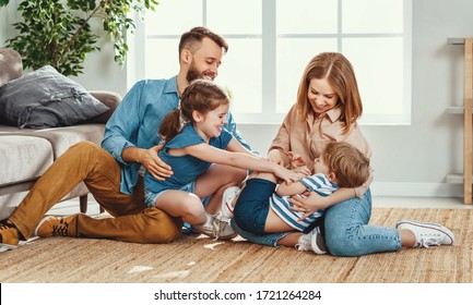 Happy Father And Mother With Little Children Sitting On Floor Near Sofa And Laughing While Having Fun Together At Home During Weekend
