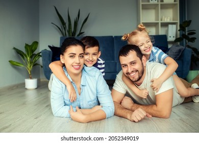 Happy father and mother with little children sitting on floor near sofa and laughing while having fun together at home during weekend  - Shutterstock ID 2052349019
