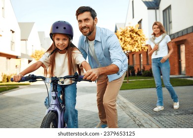 A happy father and mother taught his little daughter to ride a bicycle. A child learns to ride a bicycle. Family activities in summer. - Powered by Shutterstock