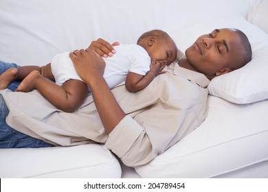 Happy father napping with baby son on couch at home in the living room
