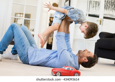 Happy Father Playing With Son While Lying On The Floor At Home. Young Man Playing With Small Boy. Flying Child Enjoying Playing With Dad.
