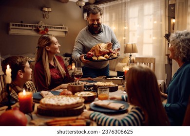 Happy father serving Thanksgiving turkey to his multigeneration family at dining table.