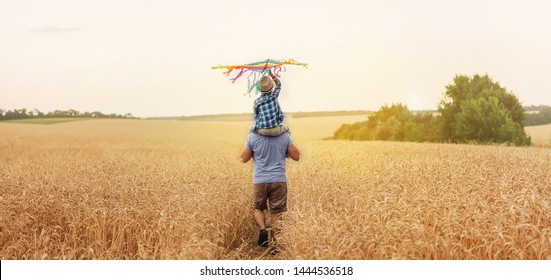 Happy father and son flying kite in the field at sunset