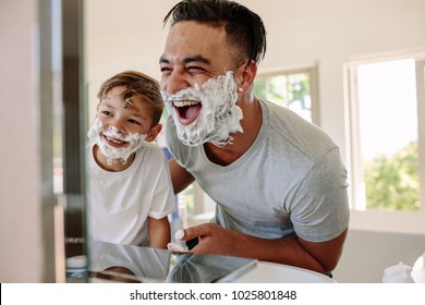 Happy father and son having fun while shaving in bathroom. Young man and little boy with shaving foam on their faces looking into the bathroom mirror and laughing. - Powered by Shutterstock