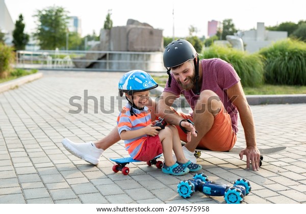 Happy father and son in helmets play in\
the Park with a robot car that is controlled by a glove while\
sitting on skateboards.\
