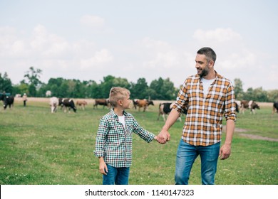 happy father and son holding hands and smiling each other at farm