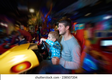 Happy Father And Son Playing Driving Wheel Video Game In Playground Theme Park