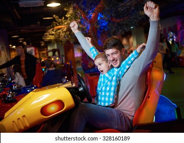 Happy Father And Son Playing Driving Wheel Video Game In Playground Theme Park