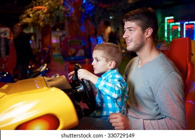 Happy Father And Son Playing Driving Wheel Video Game In Playground Theme Park