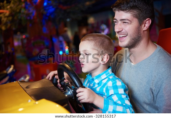 happy father and son playing driving wheel video\
game in playground theme\
park