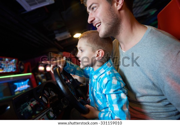 happy father and son playing driving wheel video\
game in playground theme\
park