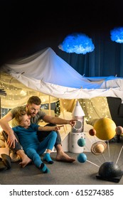 Happy Father And Son Sitting In Blanket Fort Together And Looking Away 