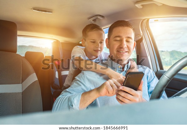 Happy father and son sitting in\
car and using smartphone in summer sunny day. Happy family\
travels