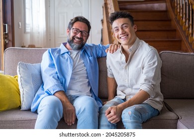 Happy father and son sitting on sofa at home. Cheerful father with teenage son sitting on couch in the living room of apartment. Portrait of father and son spending leisure time at home - Powered by Shutterstock