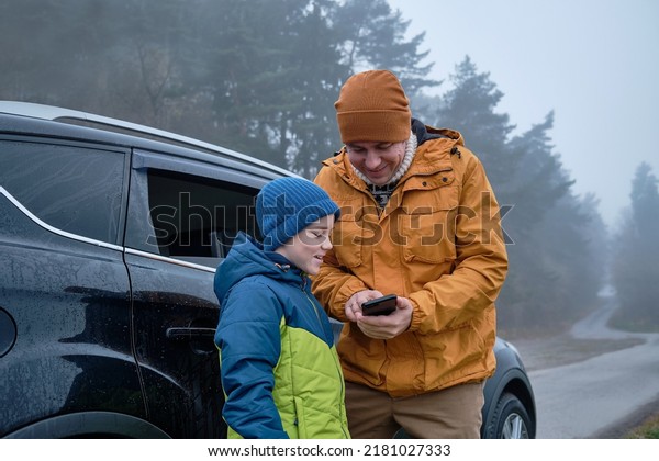 Happy\
father and son standing together near new car on a journey. Family\
are resting on the side of the road on a road trip. Child takes\
pictures on smartphone. Happy family\
travels.