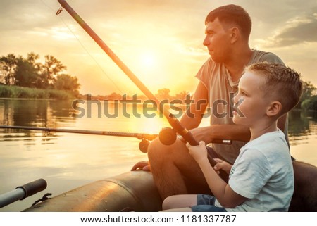Happy Father and Son together fishing from a boat at sunset time in summer day under beautiful sky on the lake.