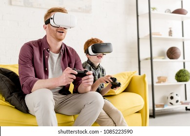 happy father and son in virtual reality headsets playing with joysticks at home - Powered by Shutterstock