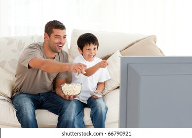 Happy father and son watching television while eating pop corn at home