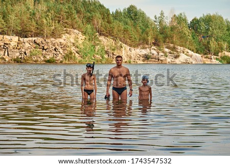 Happy father with sons in lake. Ripples on water on a background of rocky rocks. Children in underwater masks. Happy family on vacation. Father`s day.
