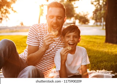 Happy father spending time with his little son at the park, eating cookies