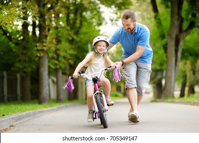 Fröhlicher Vater, der seiner kleinen Tochter beibringt, Fahrrad zu fahren. Kind, das Fahrrad fahren lernt. Familienaktivitäten im Sommer.
